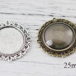 May include: Two ornate metal frames with glass inserts. The frame on the left is silver and the frame on the right is bronze. Both frames are 25 mm in diameter.