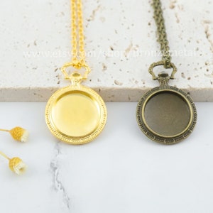 Pode incluir: Dois colares com pingente de relógio de bolso em tom dourado e bronze com correntes. Os pingentes têm um rosto redondo aberto e uma parte superior decorativa.