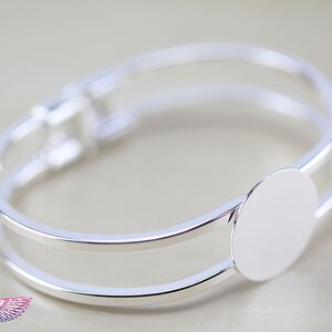 May include: Silver bangle bracelet with a round, blank, silver charm. The charm is attached to the bracelet with a hinge.