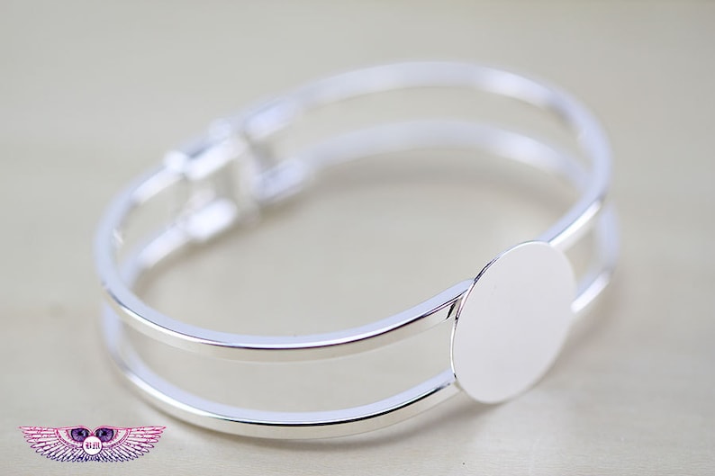 May include: Silver bangle bracelet with a round, blank, silver charm. The charm is attached to the bracelet with a hinge.