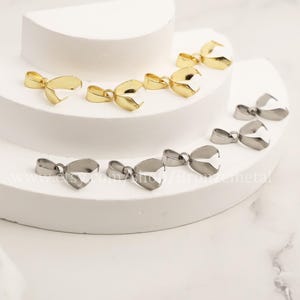 Puede incluir: Una colección de cierres de colgantes de metal dorado y plateado, también conocidos como bailes de encanto, que se muestran sobre una superficie blanca. Estos cierres se utilizan para sujetar encantos, colgantes u otros componentes de joyería a una cadena o cordón.