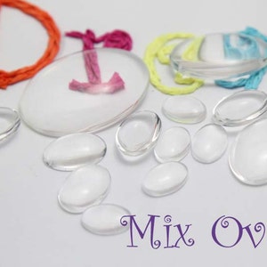 Pode incluir: Uma cole&ccedil;&atilde;o de caboch&otilde;es de vidro transparentes em forma ovalada em v&aacute;rios tamanhos. A imagem tamb&eacute;m inclui um grande caboch&atilde;o oval branco com um design rosa e laranja, e as palavras "Mix Oval" em roxo.