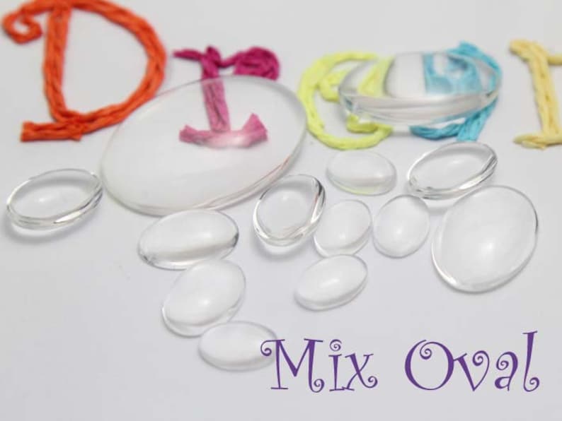 Pode incluir: Uma cole&ccedil;&atilde;o de caboch&otilde;es de vidro transparentes em forma ovalada em v&aacute;rios tamanhos. A imagem tamb&eacute;m inclui um grande caboch&atilde;o oval branco com um design rosa e laranja, e as palavras "Mix Oval" em roxo.