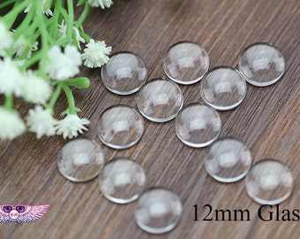 May include: A close-up of 12mm clear glass cabochons, also known as domes, on a wooden surface. The cabochons are round and have a smooth, polished finish.