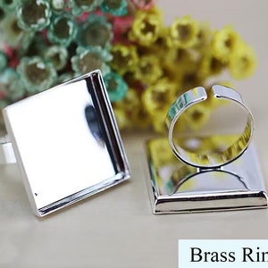 May include: Two silver-toned rings with square bezels. The bezels are empty and ready to be filled with resin or other materials. The rings are made of brass and are a popular choice for jewelry making.