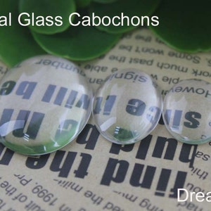Pode incluir: Tr&ecirc;s caboch&otilde;es ovais de vidro transparente de tamanhos variados. O texto "Oval Glass Cabochons" est&aacute; no topo. A palavra "Dream" est&aacute; na parte inferior. Os caboch&otilde;es t&ecirc;m texto vis&iacute;vel atrav&eacute;s deles.