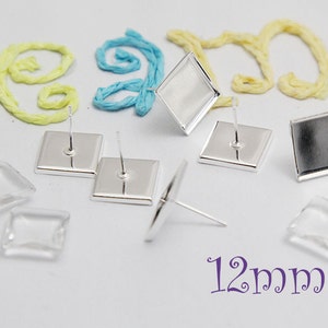 May include: Silver earring settings with clear glass square cabochons. The settings are 12mm square and have a post for attaching to an earring.