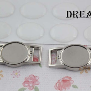 May include: Two silver metal shoe charms with a round, blank space for adding a photo or design. The charms have a slot for attaching to a shoelace.