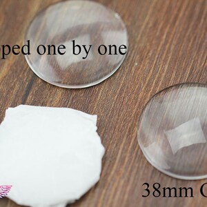 May include: Two clear glass circles, one measuring 38 mm in diameter, on a wooden surface. The text "Wrapped one by one" and "38mm Glass" are visible in the image.