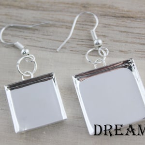 May include: A pair of silver-toned square earrings with a reflective surface. The earrings have a simple design with a hook closure. The word "DREAM" is printed in black at the bottom of the image.
