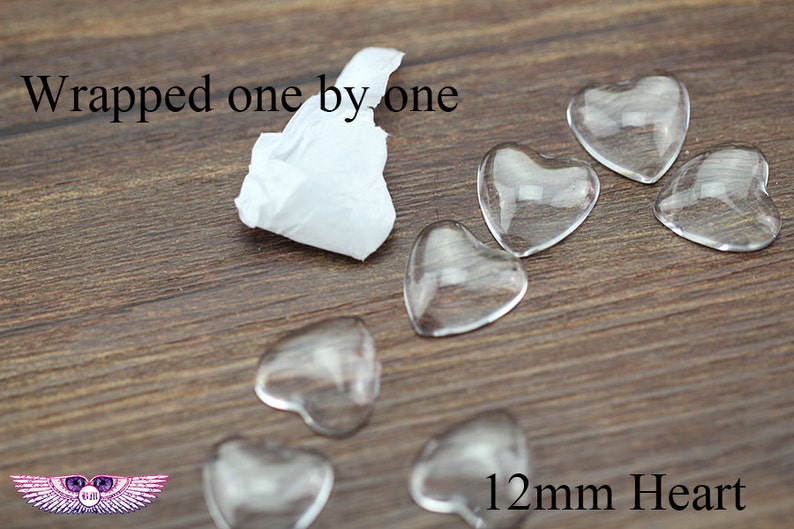 May include: Clear glass heart-shaped beads, each measuring 12mm, are scattered on a wooden surface. The text "Wrapped one by one" is visible. A small piece of white tissue paper is also present.