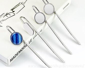 May include: Four silver metal bookmarks with different designs. One bookmark has a round blue and white stone, another has a white oval, and two have round white surfaces. The bookmarks are on a book with text.