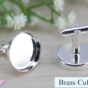 May include: A pair of silver cufflinks with round, blank, silver-toned bases. The cufflinks are made of brass and have a polished finish. Brass Cufflinks.