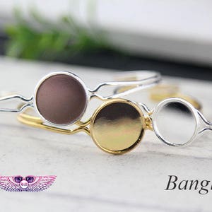 May include: A silver and gold bangle bracelet with three round glass cabochons. The cabochons are brown, gold, and clear.