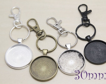 May include: Four keychains with 30mm round glass cabochon settings. The keychains are silver, black, bronze, and silver. Each keychain has a jump ring and a lobster clasp.