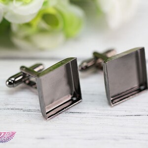 May include: A pair of silver cufflinks with square glass inserts. The cufflinks are on a white wooden surface.