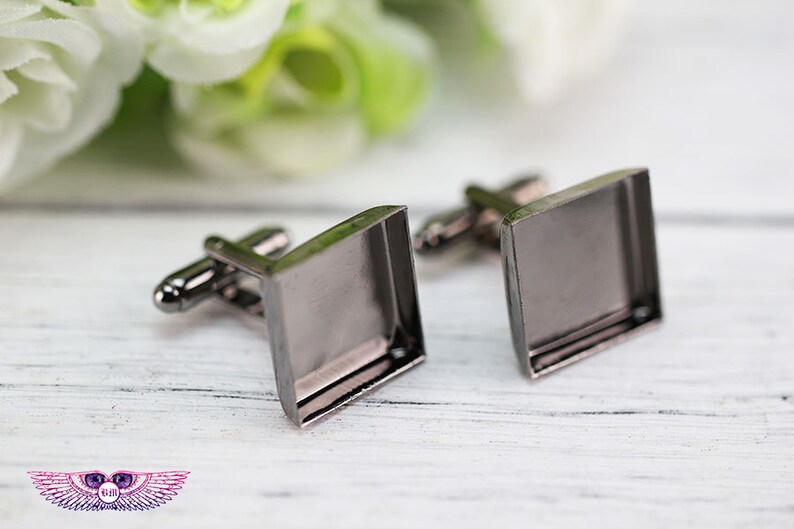 May include: A pair of silver cufflinks with square glass inserts. The cufflinks are on a white wooden surface.