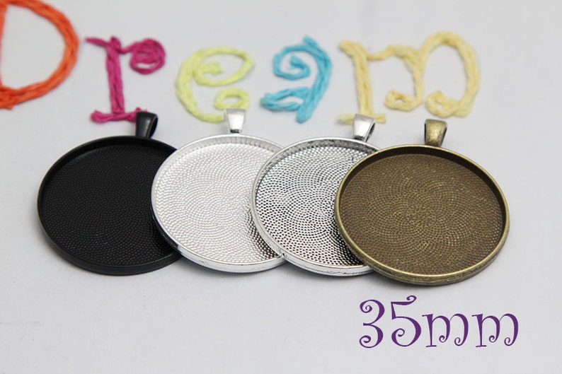 May include: Four round pendant trays in black, silver, and bronze tones. The trays are 35mm in diameter and have a textured surface. The word "dream" is spelled out in colorful yarn above the trays.