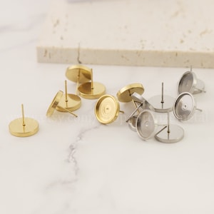 Può includere: Un set di montature per orecchini in oro e argento. Le montature sono rotonde e hanno un retro piatto. Sono progettate per contenere una varietà di cabochon.