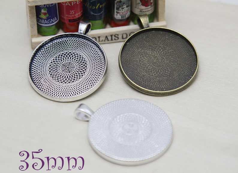 May include: Three round pendant trays in silver and bronze tones, each with a decorative patterned interior. The trays are approximately 35mm in diameter, perfect for crafting custom jewelry. The trays have a loop for attaching a chain or cord.