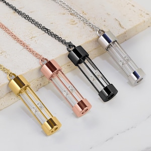 Può includere: Quattro collane con pendenti cilindrici in vetro. I pendenti hanno montature in metallo dorato, oro rosa, nero e argento. Ogni pendente è appeso a una catena abbinata. I cilindri di vetro contengono piccoli elementi decorativi.