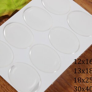 Könnte beinhalten: Ein Blatt weißes Papier mit acht durchsichtigen, runden Klebepunkten. Die Klebepunkte sind in zwei Reihen zu je vier angeordnet. Das Blatt ist mit den Größen der Klebepunkte beschriftet: 12x16mm, 13x18mm, 18x25mm und 30x40mm.