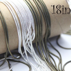 May include: A close-up of a variety of silver and bronze snake chains, all 18 inches long, wrapped around a cardboard tube.