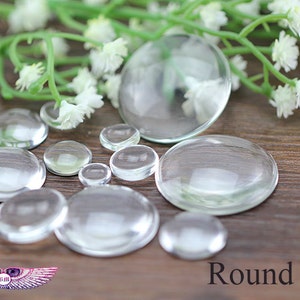 May include: Assortment of clear glass cabochons of various sizes, arranged on a wooden surface. The cabochons are round and have a smooth, polished finish. The text "Round Mix" is visible in the lower right corner of the image.