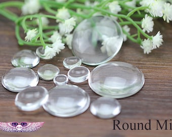 May include: Assortment of clear glass cabochons of various sizes, arranged on a wooden surface. The cabochons are round and have a smooth, polished finish. The text "Round Mix" is visible in the lower right corner of the image.