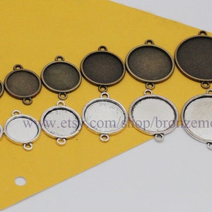 Puede incluir: Surtido de bandejas redondas de metal para colgantes de varios tamaños. Las bandejas son de color plateado y bronce y tienen tres bucles en la parte superior para colgar. Las bandejas están dispuestas en orden de tamaño, de la más pequeña a la más grande.