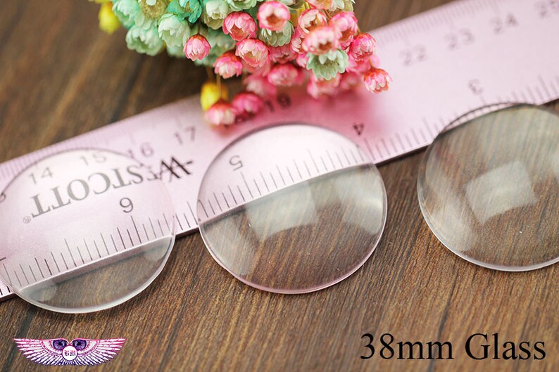May include: Two clear glass circles, each measuring 38 mm in diameter, are placed on a wooden surface. A pink ruler with black markings is partially visible behind the circles.
