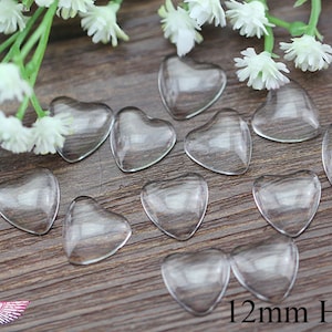 May include: Clear, heart-shaped glass beads, each measuring 0.47 inches, are scattered on a wooden surface. White flowers and greenery are in the background. The image includes the text "12mm Heart".