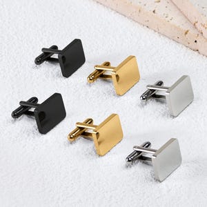 May include: A collection of six rectangular cufflinks arranged in two rows. The set includes two matte black cufflinks, two polished gold-tone cufflinks, and two polished silver-tone cufflinks, each featuring a standard swivel toggle backing.