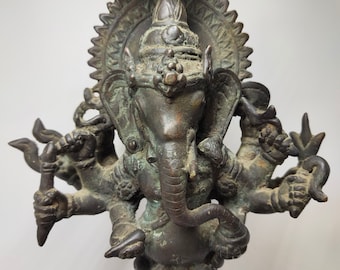 Op de afbeelding: Een bronzen beeld van Ganesha, de hindoeïstische god van wijsheid en voorspoed, met meerdere armen en een groot hoofd. Het beeld is ingewikkeld gedetailleerd en heeft een donkere patina.