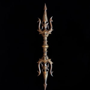 May include: A double-ended bronze vajra featuring intricate relief carvings of floral motifs and stylized faces on both ends. The central handle is cylindrical with tiered, decorative bands, and the metal has a dark, aged patina finish.