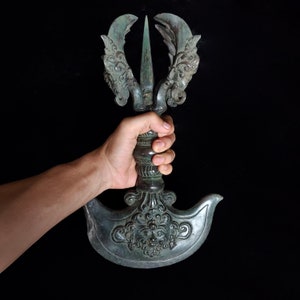 May include: A bronze ceremonial weapon with intricate carvings and a sharp blade. The weapon has a handle with a decorative design and a large, curved blade.
