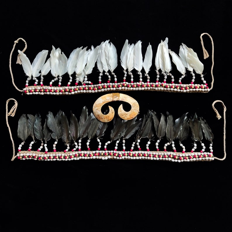 May include: Two feather necklaces with beaded detailing and a bone pendant. One necklace has white feathers, the other black. The beads are white and red. The pendant is a light tan colour and has a curved shape.