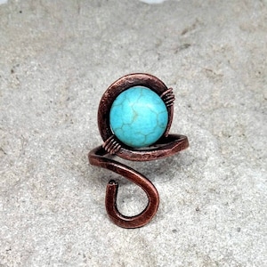 Può includere: Un anello in filo di rame con una pietra turchese incastonata in un cerchio di filo di rame.