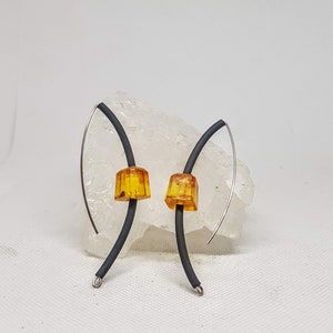 Może przedstawiać: Para kolczyków z czarnym drutem i bursztynowymi szklanymi koralikami. Kolczyki są prezentowane na białym tle.