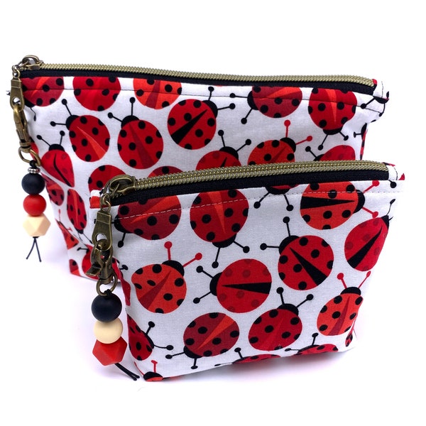 Trousse à maquillage coccinelle, entièrement doublée, légèrement rembourrée. Coccinelles rouges et noires sur fond blanc, fermeture à glissière avec tirette en perles. 2 tailles disponibles.