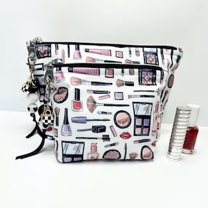 Lustige Make-up-Thema Reißverschlusstasche, komplett gefütterte, leicht gepolsterte Tasche zur Organisation Ihrer Beauty-Produkte. Lippenstift Charm Anhänger an einem Schwarz & Silber Reißverschluss.