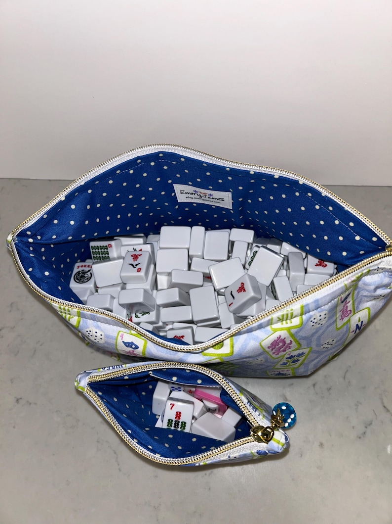May include: Two zippered pouches, one large and one small, filled with white Mahjong tiles. The pouches have a blue polka dot lining and a light blue exterior with a floral and character design. The small pouch contains dice.