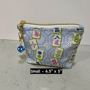 May include: Small, light blue zippered pouch with a gold zipper and a blue die charm. The pouch features a pattern of Mahjong tiles and dice. The pouch measures 6.5 inches by 5 inches.