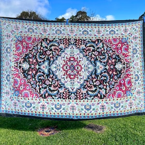Könnte beinhalten: Ein schwarzer Wandteppich mit einem bunten Blumenmuster. Der Wandteppich hat ein zentrales Medaillon mit einem rot-weiß-blauen Design. Der Wandteppich hängt an einer Wäscheleine.