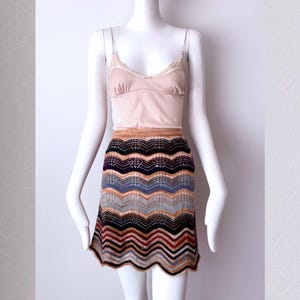 May include: A mannequin displays a multi-colored chevron pattern skirt with a scalloped hemline. The skirt features a palette of brown, black, blue, and orange hues. It is paired with a light pink camisole with lace trim.