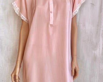May include: A light pink knee-length nightgown featuring short sleeves with white lace trim, a round neckline, and a partial front button placket with three matching pink buttons. The garment includes vertical pleat detailing at the shoulders.