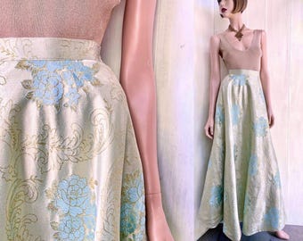 May include: A floor-length skirt featuring a metallic gold base with a light blue floral and scrollwork pattern. The skirt has a high waistband and a full, flowing silhouette. It is paired with a sleeveless, solid tan top with a V-neckline.