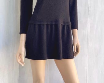 May include: Black knit dress with a beaded collar and a small pocket. The dress has three-quarter sleeves and a flared skirt. A black hat is also visible.