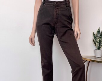 May include: A pair of dark brown denim jeans featuring a high-waisted fit, a button and zipper fly closure, and classic five-pocket styling. The jeans have a straight-leg silhouette and are paired with a plain white short-sleeved v-neck t-shirt.