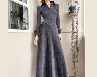 May include: A long-sleeved, floor-length dress in a dark charcoal gray metallic knit fabric. The bodice features a button-down front with a pointed collar, while the skirt flares into a wide, A-line silhouette. The cuffs are finished with buttons.